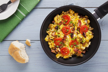 Scrambled eggs in a pan with bacon, onion and tomatoes sprinkled