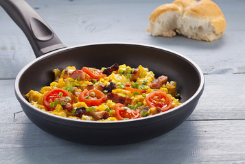 Scrambled eggs in a pan with bacon, onion and tomatoes sprinkled