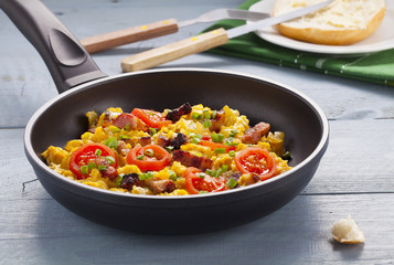 Scrambled eggs in a pan with bacon, onion and tomatoes sprinkled