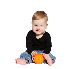 smiling baby sits and holds orange in hands 