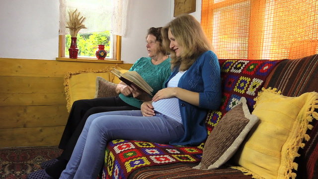 young woman strokes pregnant belly, reading book with grandma