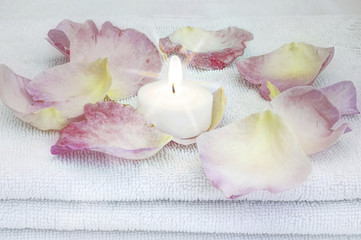 weisse brennende Kerze inmitten von Rosenblaettern