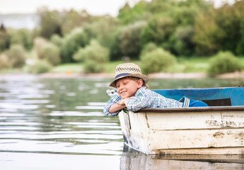 Little boy in old boat on the calm lake surface