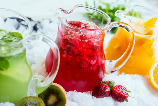 a mix of several bright colored delicious cold lemonade carafes