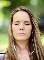 Naklejka premium Female student girl outside in park listening to music on headph