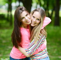 Fototapeta premium Two young girl friends in a hug at park