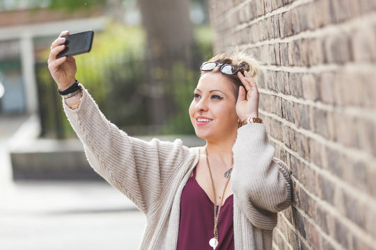 Hipster woman taking a selfie against brick wall in London.