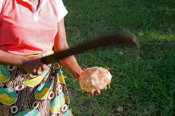 African woman opens coconut with a machete.