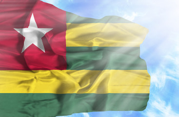 Togo waving flag against blue sky with sunrays