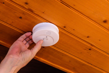 Hand installing Smoke detector on wood ceiling inside the house