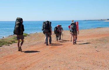 group of tourists with large backpacks are on road to the sea