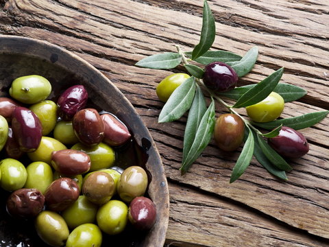 Wooden bowl full of olives and olive twigs besides it.