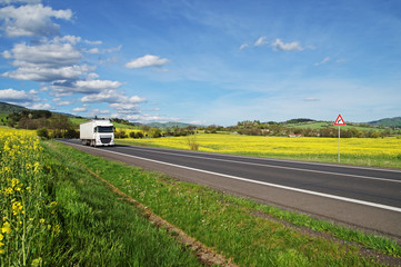 White truck driving on the road between rapeseed field