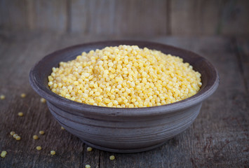 Dry Israeli couscous ptitim in a clay bowl on wooden table