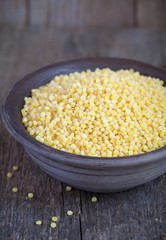 Dry Israeli couscous ptitim in a clay bowl on wooden table