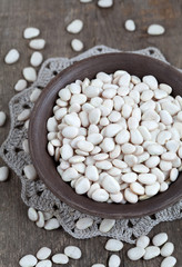 Dry white baby lima beans in a clay bowl on wooden table