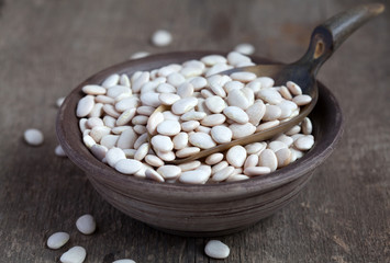 Dry white baby lima beans in a clay bowl on wooden table