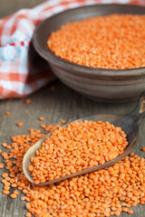 Dry red lentils in a clay bowl and in a scoop on wooden table