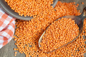 Dry red lentils in a clay bowl and in a scoop on wooden table