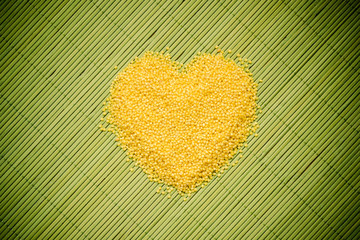 Millet groats heart shaped on green mat surface.