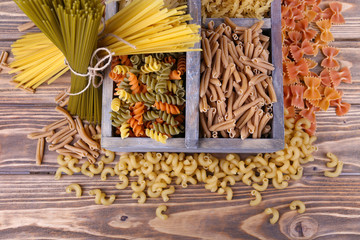 Different types of pasta in box on wooden background