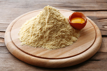 Heap of flour on cutting board with egg on wooden table