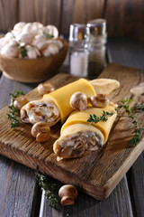 Pancakes with creamy mushrooms on cutting board on wooden table, closeup