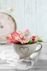 Beautiful flowers in cup, on wooden background