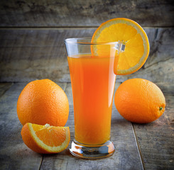 Orange juice glass and fresh oranges on wood