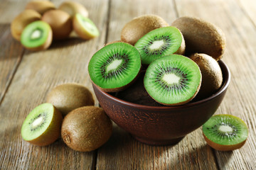 Juicy kiwi fruit in bowl on wooden background