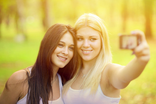 Outdoor portrait of two girl friends taking photos with camera