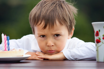 Close-up portrait of angry little boy with a cake and tea
