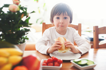 Beautiful little boy, eating sandwich at home, vegetables on the
