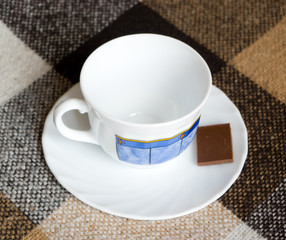 Empty tea cup with piece of milk chocolate on a brown  plaid  