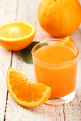 Orange fruit and glass of juice on white wooden background