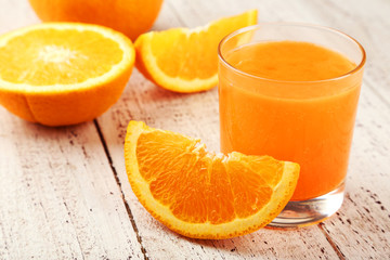 Orange fruit and glass of juice on white wooden background