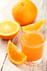 Orange fruit and glass of juice on white wooden background