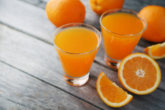 Glass of fresh orange juice on grey wooden background