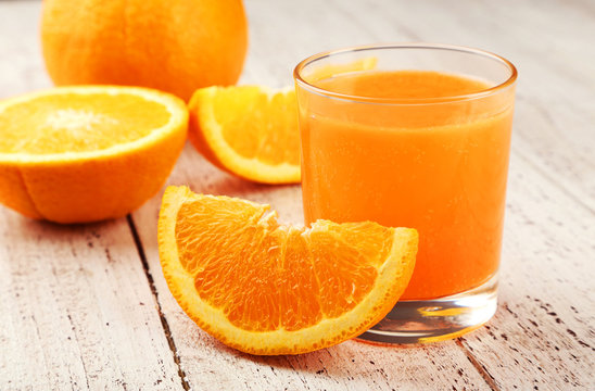 Orange fruit and glass of juice on white wooden background