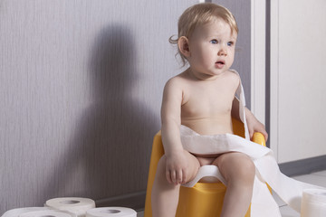 Cute baby sitting on chamber pot with toilet paper