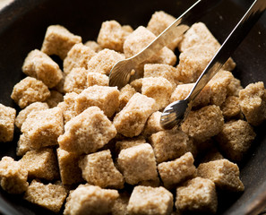 Cubes of cane sugar in the bowl on wooden table.