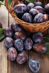 Fresh plums in basket on brown wooden background