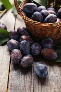 Fresh plums in basket on brown wooden background