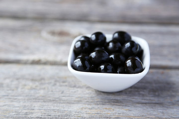 Black olives in bowl on grey wooden background