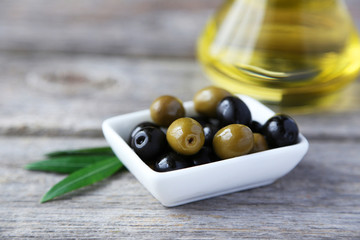 Green and black olives in bowl on grey wooden background