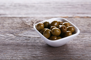 Green olives in bowl on grey wooden background