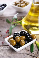 Green and black olives in bowl on grey wooden background