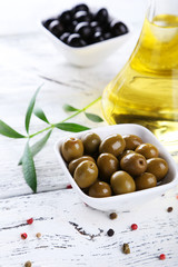 Green and black olives in bowl on white wooden background
