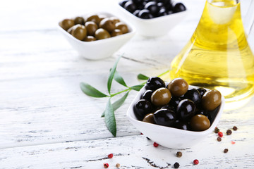 Green and black olives in bowl on white wooden background