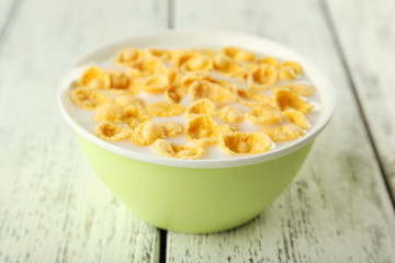 Bowl of cornflakes with milk on white wooden background